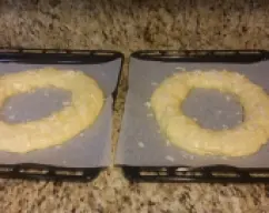 Step <p>Con las manos aceitadas, saca la masa del vaso, divídela en dos, haz dos bolas y forma los roscones haciendo un agujero en el centro y estirando la masa para darle forma en una hoja de papel para hornear, ten en cuenta que crece bastante, estira la masa lo suficiente que no se junte en el centro. Pinta con huevo batido y ponle por encima azúcar humedecido y almendra laminada. Puedes ponerle guindas, fruta confitada...</p> illustration